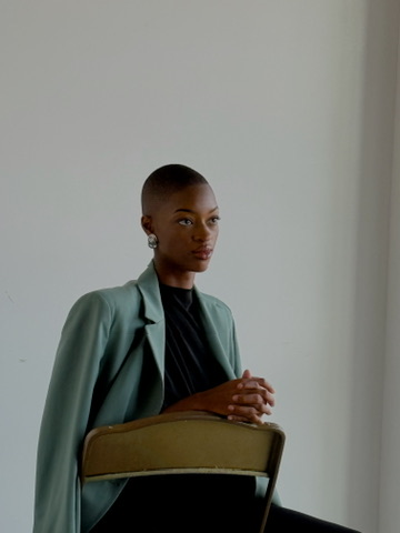 Model in a sage green blazer seated on a vintage chair
