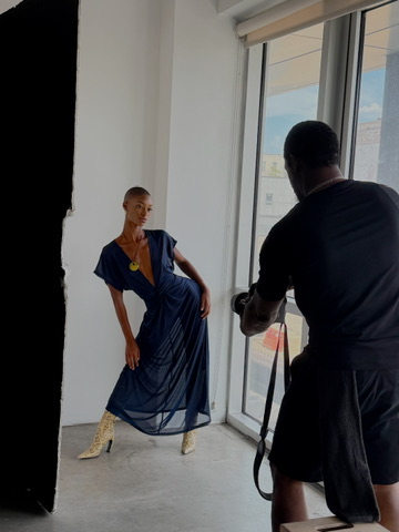 Behind the scenes: model in a navy chiffon dress and gold boots being photographed
